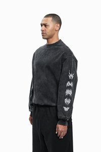 Sudadera negra con una textura suave y desgastada. Presenta diseños gráficos blancos a lo largo de la manga izquierda y un cuello redondo clásico. Combinada con pantalones oscuros.