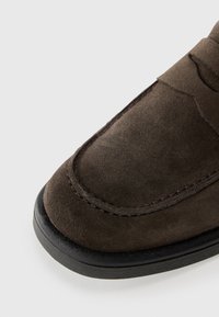 Tumši brūni zamšādas loafers ar noapaļotu purngalu un šuvju apdari pa malu. Zole ir izgatavota no melnas gumijas, nodrošinot papildu saķeri un izturību.
