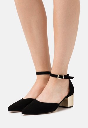 Chaussures à brides autour de la cheville en daim noir avec un bout pointu et un talon bloc doré épais. Dotées d'une fine boucle pour un ajustement réglable.