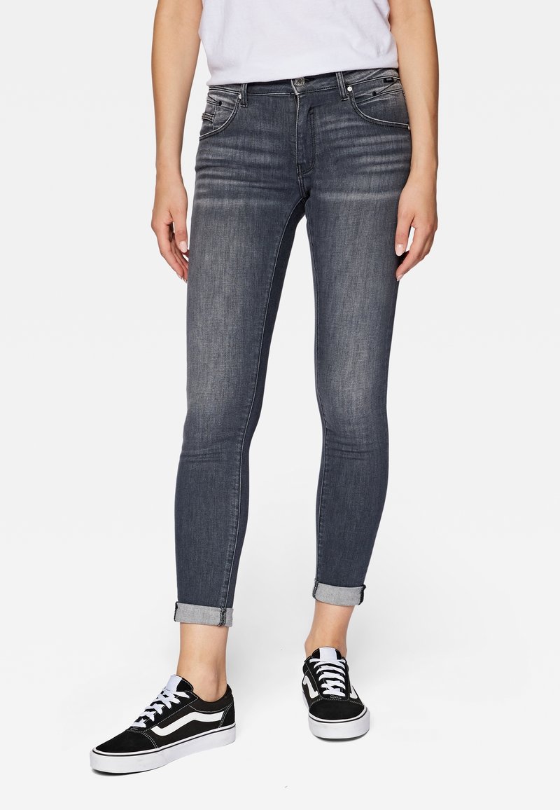 Smal denimjeans i grått med ljus blekning, uppvikta fållar och fem fickor, kombinerade med svarta sneakers med vita detaljer.