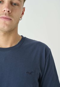 Marineblaue Baumwoll-T-Shirt mit Rundhalsausschnitt und kurzen Ärmeln. Verfügt über ein kleines gesticktes Logo auf der Brust. Glatte Textur.