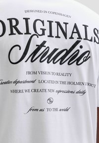 Λευκή βαμβακερή μπλούζα Τ-shirt με μαύρο εκτυπωμένο κείμενο. Ο σχεδιασμός περιλαμβάνει φράσεις όπως "ΣΧΕΔΙΑΣΜΕΝΟ ΣΤΗΝ ΚΟΠΕΓΧΑΓΗ" και "ΑΥΘΕΝΤΙΚΑ Studio" εμφανώς τοποθετημένες.