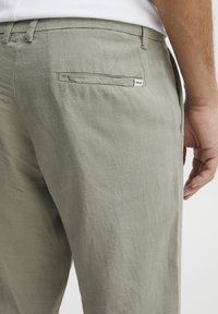 Light gray linen pants with a straight cut, featuring a subtle texture and a single back pocket with a logo tag. Side hand pockets visible.