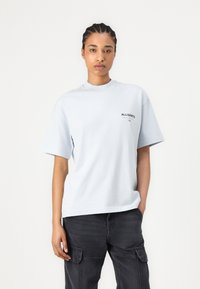 Lyseblå oversized t-skjorte i bomull med korte ermer og rund halslinning. Har en liten svart logo på venstre bryst.