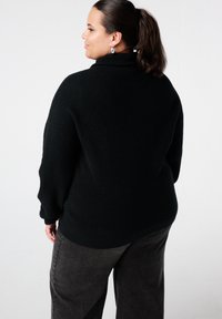 Zwarte geribbelde coltrui met een losse pasvorm, voorzien van lange mouwen en een hoge hals, gecombineerd met donkere wijd uitlopende broek.