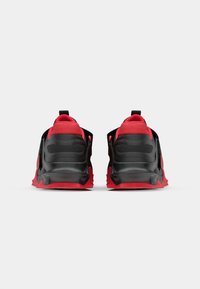 Black and red athletic shoes with a textured mesh upper, curved sole, and pull tabs, featuring a prominent heel and supportive ankle design.