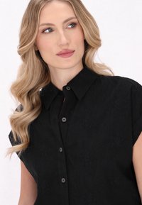 Cămașă scurtă neagră cu guler butonat, având un model floral texturat și nasturi negri, creând un design subtil și elegant.