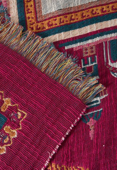 Tissu rouge tissé avec des franges multicolores et des motifs géométriques en tons jaunes, bleu sarcelle et crème, superposé à un tissu à motif similaire.