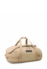 Sac de sport beige en tissu durable. Dispose de poignées doubles, d'une poche zippée et du logo "THULE" affiché de manière bien visible.