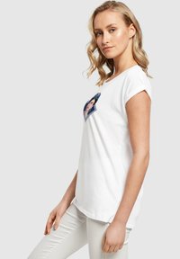 Hvid bomulds T-shirt med oprettede ærmer, der har et farverigt Frida Kahlo grafik foran. Klassisk fit med rund halsudskæring.