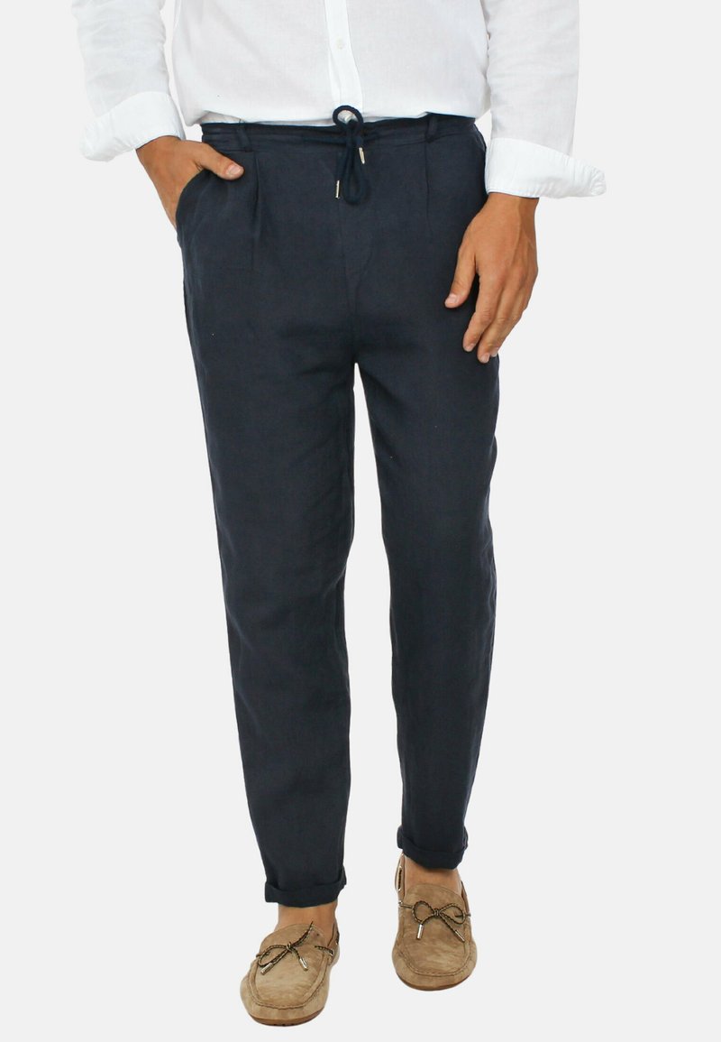 Pantaloni in lino blu navy con vita regolabile, fit affusolato, due tasche laterali e orli risvoltati. Abbinati a mocassini color beige chiaro.