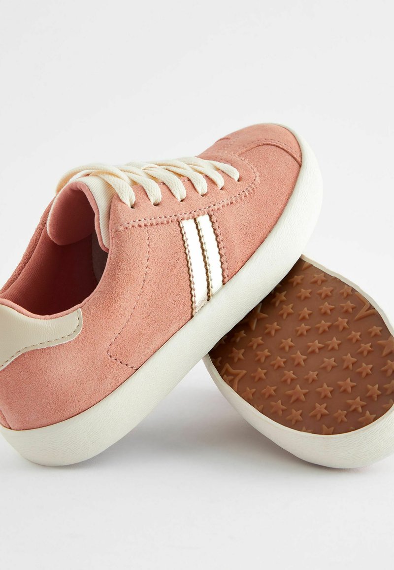 Zapatillas de ante rosa con cordones y franjas blancas. La suela de goma presenta un patrón de estrellas. La parte trasera tiene un acento beige contrastante.