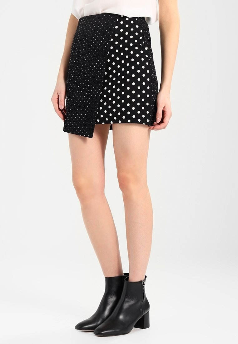 Černobílá sukně s puntíky a asymetrickým designem; obsahuje kombinaci velkých a malých puntíků. Nosit s černými kotníkovými botami.