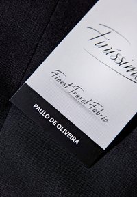 Czarna tkanina podróżna o teksturowanej powierzchni, z białą metką, na której widnieje napis „Finissino” oraz „Finest Travel Fabric” napisany kursywą.