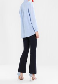 Camicia a maniche lunghe azzurro chiaro con colletto, abbinata a pantaloni svasati scuri e scarpe con tacco azzurro chiaro.