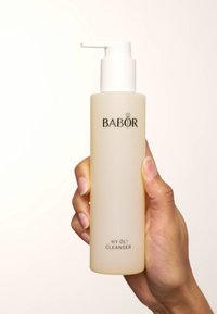 Bouteille transparente de nettoyant BABOR HY-ÖL. Texture lisse, légèrement givrée avec un couvercle à pompe blanc. Lettres noires à l'avant.