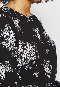 Musta kangasmekko, jossa valkoinen kukkakuvio, pyöreä pääntie ja olkapäällä rypytetty yksityiskohta. Kevyt ja teksturoitu materiaali.