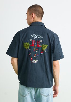 Short-sleeve navy shirt featuring colorful embroidered scene on back with figures, trees, and speakers; relaxed fit with a casual style.