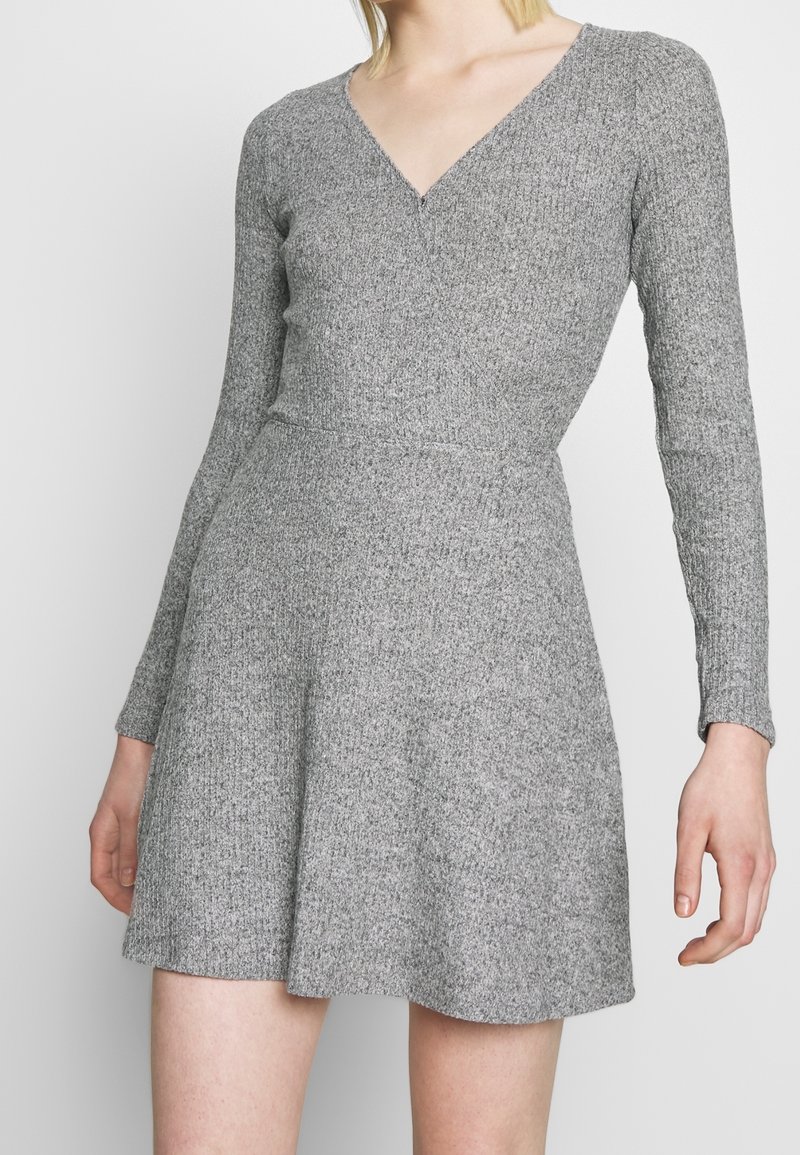 Robe grise à manches longues en texture côtelée avec un décolleté en V et un corsage ajusté, s'évasant en jupe, offrant un look confortable et décontracté.