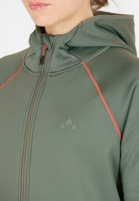 Grön zip-up hoodie med orange sömmar, hög krage och logodetalj. Mjuk tyg med slät struktur och figurnära design.