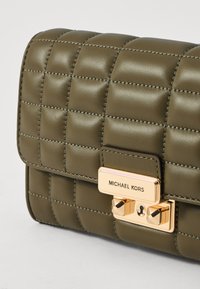 Borsa a tracolla in pelle verde oliva con design trapuntato, hardware in tonalità oro e una chiusura prominente con il nome del marchio. Dettagli di superficie testurizzata.