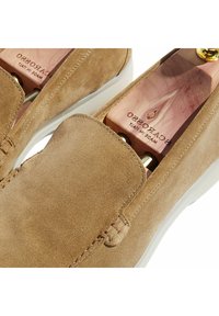 Mocassini in suede beige con design slip-on, caratterizzati da una texture morbida, cuciture decorative e una suola in gomma di colore chiaro.