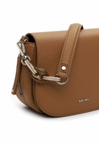 Bolso bandolera de cuero marrón con textura granulada, forma redondeada, herrajes plateados y un adorno de eslabones decorativos en cadena. Incluye un bolsillo lateral con cremallera.