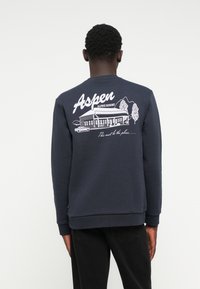 Marineblauwe sweatshirt met een grafisch ontwerp van een resort met bergen, bomen en een auto. Inclusief de tekst "Aspen Alpine Resort". Klassieke pasvorm.