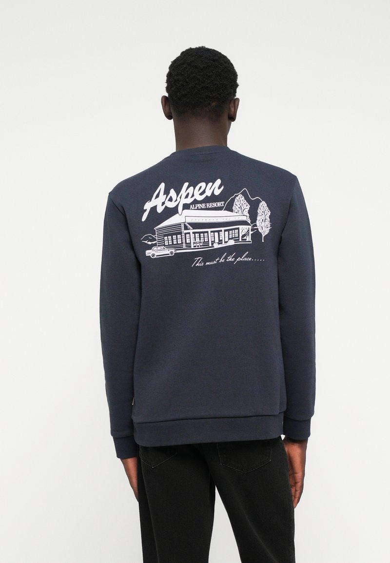 Marineblauwe sweatshirt met een grafisch ontwerp van een resort met bergen, bomen en een auto. Inclusief de tekst "Aspen Alpine Resort". Klassieke pasvorm.