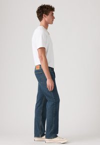 Blauwe denim jeans met een rechte snit, subtiele wassing en een tan leren label op de achterkant. Gecombineerd met een eenvoudig wit t-shirt.