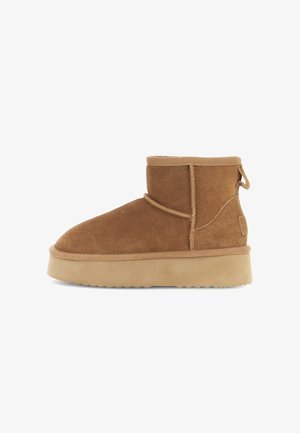 Botine din suede brown cu o talpă groasă din cauciuc bej, detalii cusute și un tab pentru a le trasa pe călcâi.