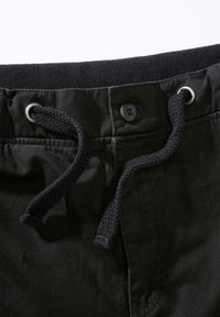 Juodos kelnės su raišteliais liemens srityje, metaliniais žiedais ir švelnios tekstūros audiniu. Turi sagos užsegimą ir kontrastingus siūlus.