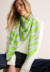 Grøn og grå mønstret tørklæde med en blød tekstur, stor trekantet form, draperet løst omkring halsen mod en lys sweater.