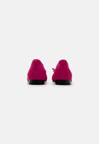 Zapatos de ante rosa con punta redondeada y tacón bajo negro, con un lazo en la parte trasera. Textura suave con un acabado uniforme.