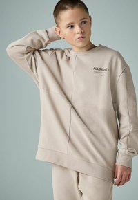 Beige oversize džemperis ar ribotu tekstūru, garām piedurknēm un diskretu logotipu krūtīs. Iezīmē relaksētu piegriezumu un nokritušiem pleciem.