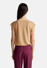 Krátký rukáv, zlatohnědý top z měkké tkaniny, kombinovaný s švestkovými kalhotami s zadními kapsami a na míru střiženým střihem.