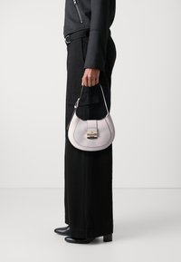 Mała, zakrzywiona torebka w jasnolawendowym skórzanym wykończeniu z złotą klamrą i górnym uchwytem; noszona z czarnymi szerokimi spodniami i czarnymi botkami za kostkę.