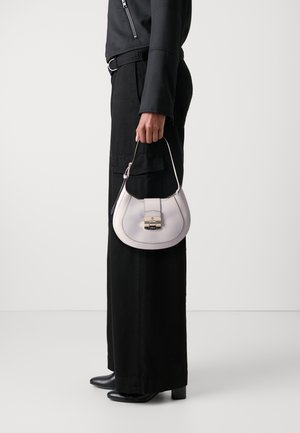 Petit sac à main courbé en cuir lavande clair avec un fermoir en or et une poignée supérieure; porté avec un pantalon large noir et des bottines noires.