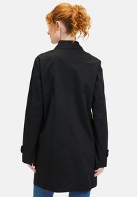 Schwarzer Trenchcoat mit geradem Design, langen Ärmeln und geknöpften Manschetten. Glatte Textur, Rückennahtdetails und Kragen vorhanden.