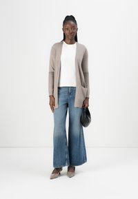 Beige stickad kofta över en vit topp, i kombination med vida ljusblå jeans. Outfitten fulländas med grå klackar och en svart handväska.