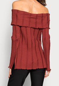 Red ribbed off-the-shoulder top with a flared neckline and long sleeves, featuring a textured finish and side slits at the hem.