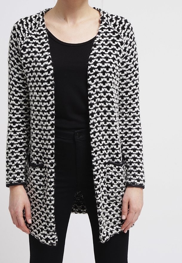 Long cardigan à motif noir et blanc porté sur un haut noir et un pantalon noir, montré des épaules aux hanches.