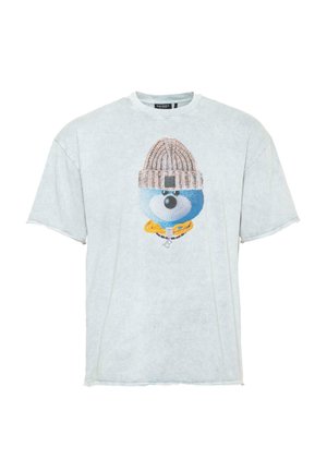 Helehall oversized T-särk, millel on sinine joonistatud näo graafika, millel on kudumisest beež beanie ja kollased aksessuaaride detailid.