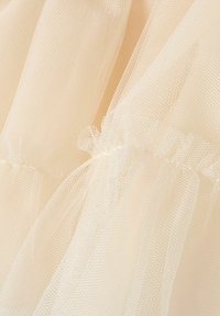 Svetlo bež til tkanina z fino mrežasto strukturo, nabran na intervalih, z nabrano robovi za dodatne podrobnosti.