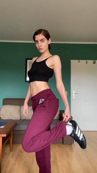 Black ribbed crop top paired with maroon athletic pants featuring a logo, and black sneakers with white stripes. Background has green wall.