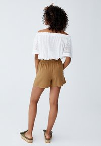 Haut blanc décolleté épaules avec des accents en dentelle, associé à un short marron avec une taille élastique. Porté avec des chaussures vertes à enfiler.