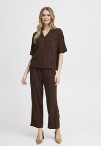 Ensemble deux pièces marron comprenant une chemise à manches courtes avec un bouton et une poche, ainsi que un pantalon ample avec des ourlets repliés.