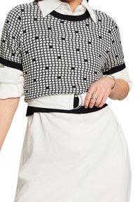 Top de punto con estampado en blanco y negro, de manga corta, cuello redondeado y bordes acanalados, combinado con una falda blanca y un cinturón con hebilla circular.