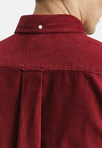Rode corduroy overhemd met verticale ribbels, een puntkraag en een rugplooi met een enkele knoopsluiting bij de hals.