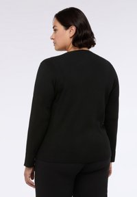 Černý dlouhý rukáv top s kulatým výstřihem, měkkou texturou, přiléhavým střihem a minimálním designem, kombinovaný s černými kalhotami.